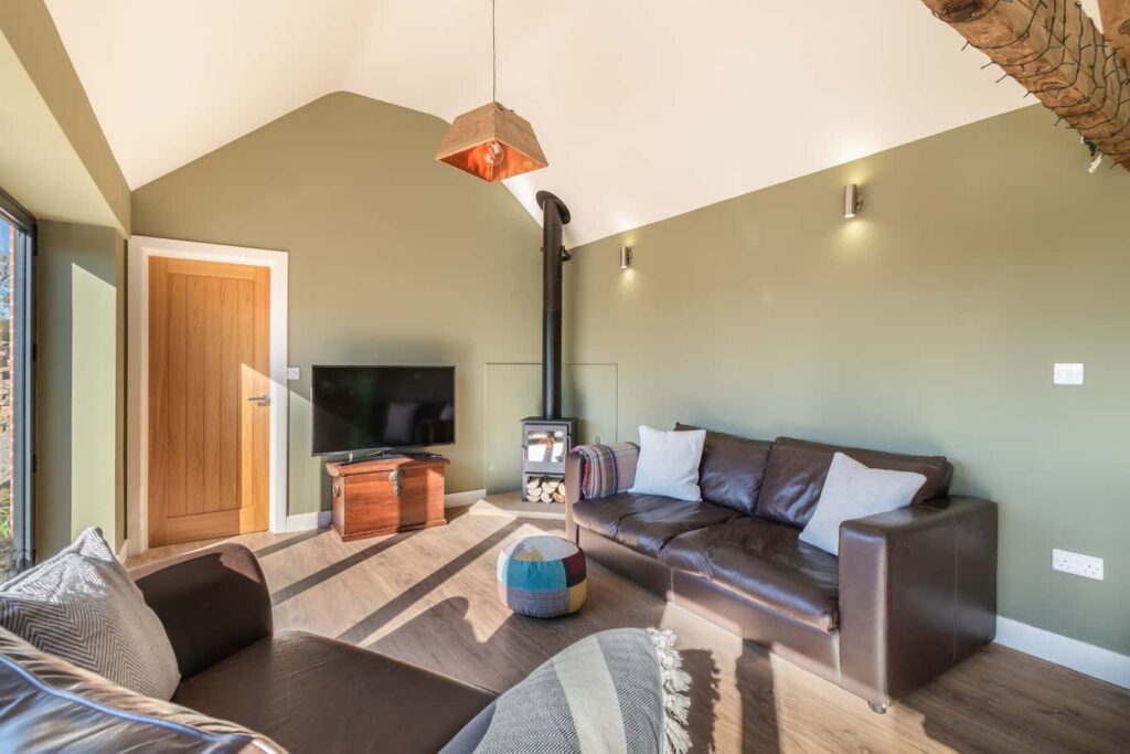 Green End Farms Sheep Shed Open sitting area with a large leather couch, big-screen tv and a wood-burning fireplace
