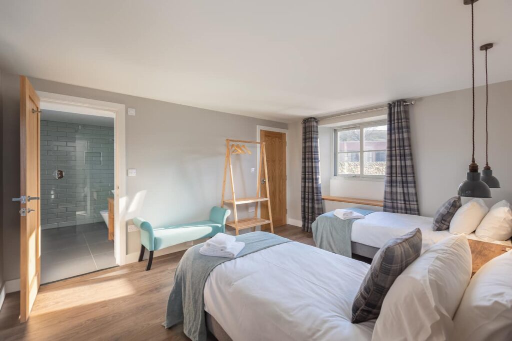 The Stables bedroom 2 with 2 single beds and view of ensuite bathroom