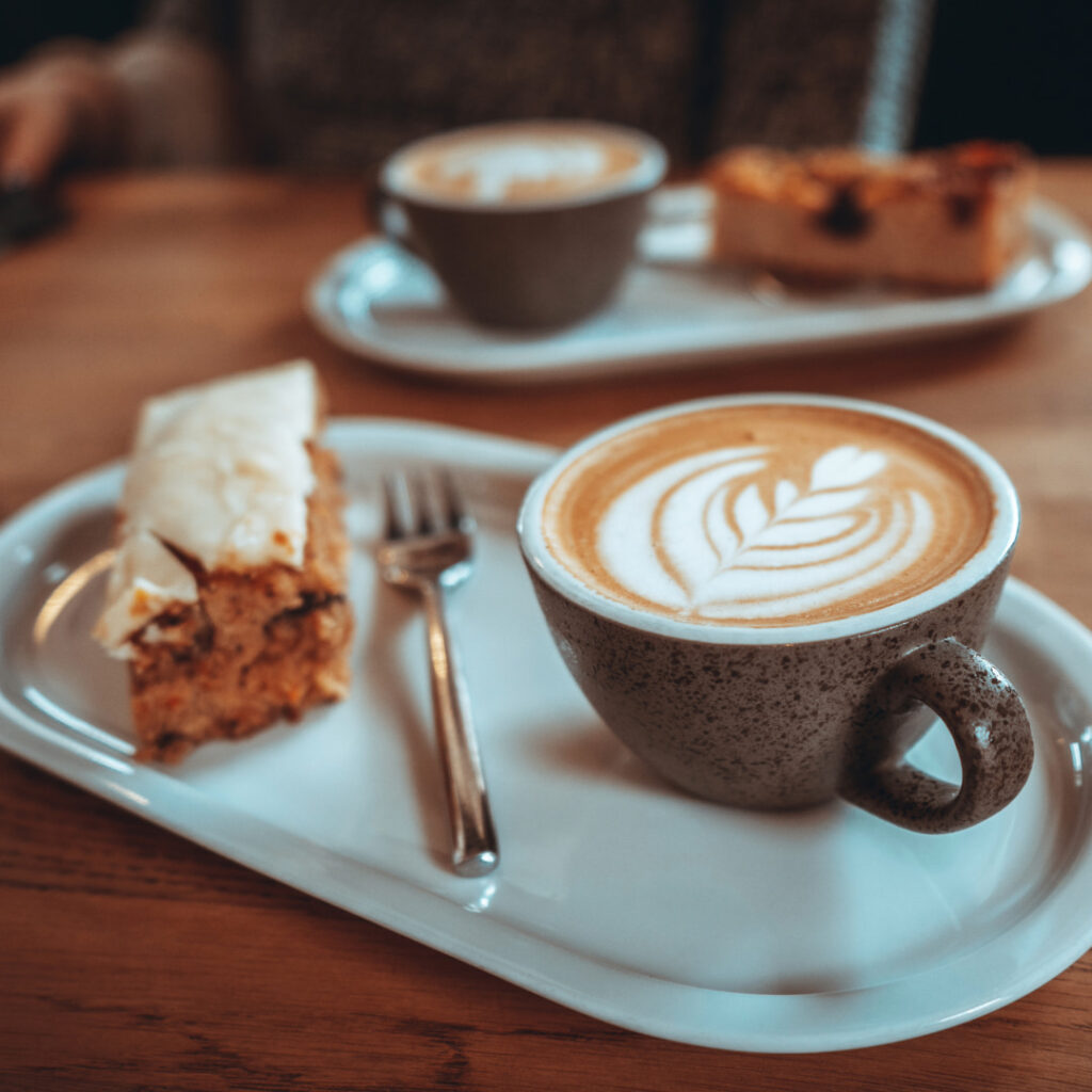 closeup of artfully-made cappuccino in stoneware cup next to a slice of cake