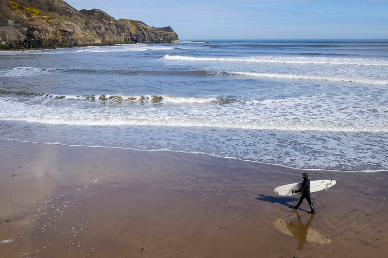 surfer in full wetsuit walking on the beach with board